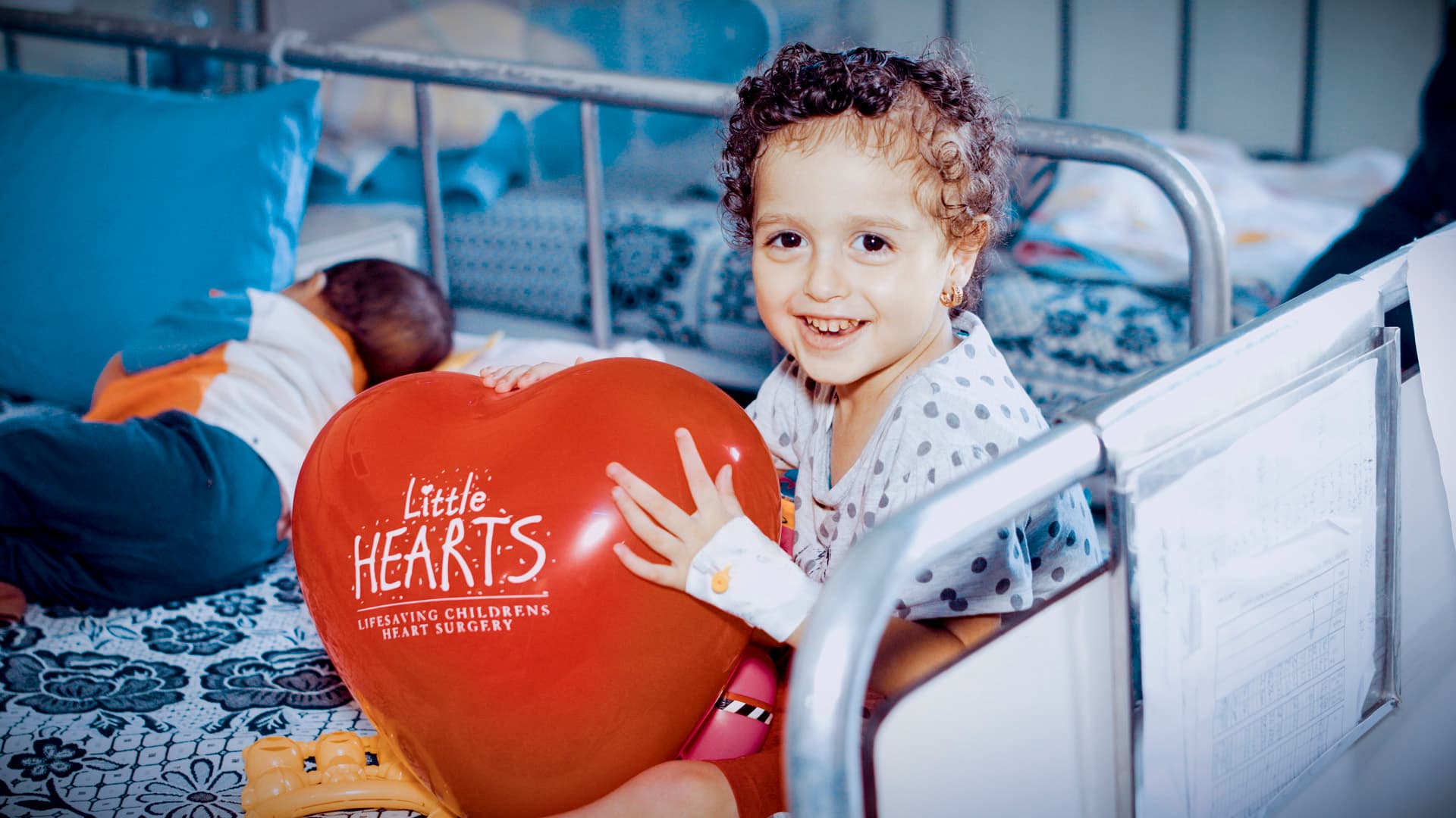 A smiling girl holding a Little Hearts balloon