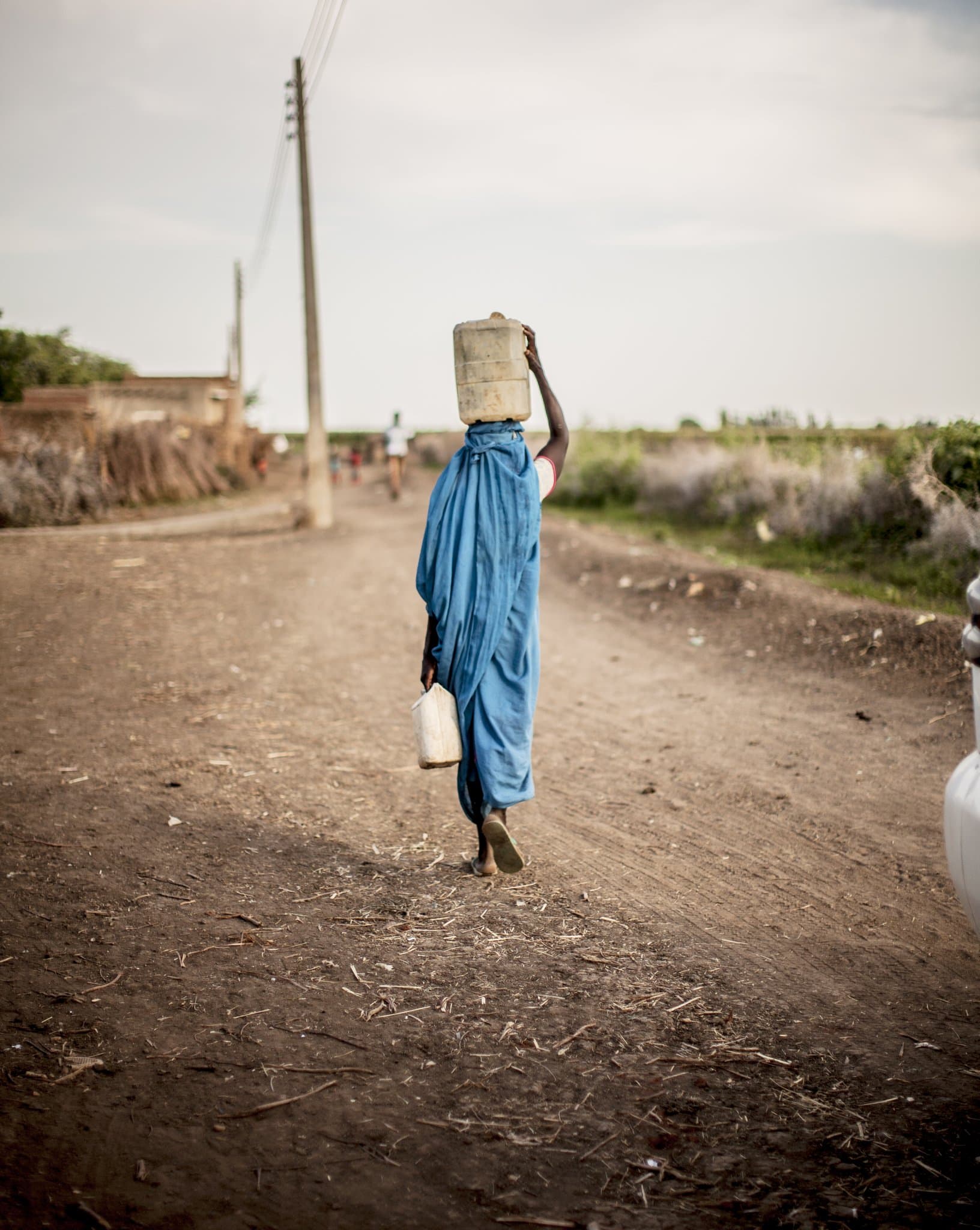 A woman carrying water home along a dirt road